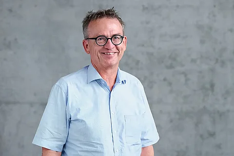 Portrait von Alfred Steimer, der ein hellblaues Hemd trägt, vor Beton-Hintergrund