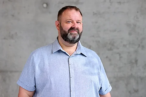 Portrait von Martin Raab, der ein hellblaues Hemd trägt, vor Beton-Hintergrund